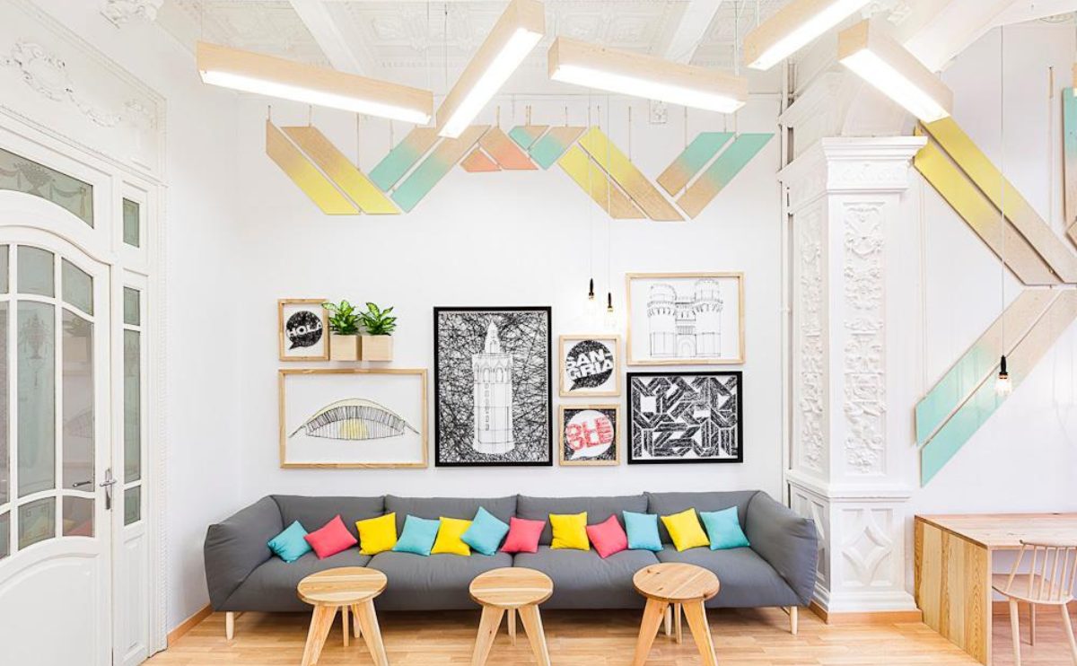 スペイン、バレンシアのスペイン語学校、AIL Valenciaの待合ロビーのソファに、ピンク、黄色、水色の色鮮やかなクッションが置かれ、壁には現代アートのような大小異なる大きさの絵が7枚かかっている