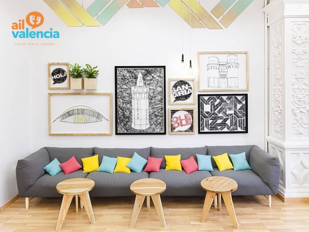スペイン、バレンシアのスペイン語学校、AIL Valenciaの待合ロビーのソファに、ピンク、黄色、水色の色鮮やかなクッションが置かれ、壁には現代アートのような大小異なる大きさの絵が7枚かかっている